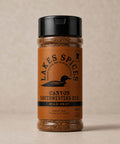 A 5oz bottle of Lake Spices Canyon Southwestern Rub, featuring the company logo of a black loon on an orange-brown background, and a black icon of Minnesota in the upper righthand corner. Label text above the loon reads “Lake Spices: Honest Blends for Homemade Taste.”