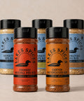 Five bottles of Lake Spices Rubs, one of each flavor, in two staggered lines: Foundry Original BBQ Rub, Canyon Southwestern Rub, Signature SPG Rub, Signature SPG Rub (Hickory Smoked), and Signature SPG Rub (Applewood Smoked)