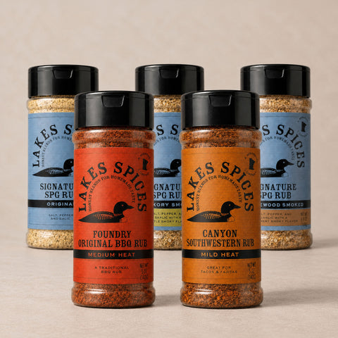 Five bottles of Lake Spices Rubs, one of each flavor, in two staggered lines: Foundry Original BBQ Rub, Canyon Southwestern Rub, Signature SPG Rub, Signature SPG Rub (Hickory Smoked), and Signature SPG Rub (Applewood Smoked)