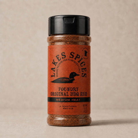 A 5oz bottle of Lake Spices Foundry Original BBQ Rub, featuring the company logo of a black loon on an orange background, and a black icon of Minnesota in the upper righthand corner. Label text above the loon reads “Lake Spices: Honest Blends for Homemade Taste.”