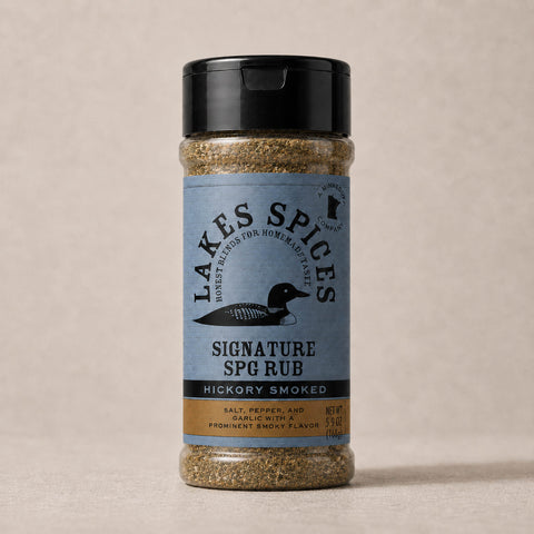 A 6oz bottle of Lake Spices Hickory Smoked Signature SPG Rub, featuring the company logo of a black loon on a blue-grey background, and a black icon of Minnesota in the upper righthand corner. Label text above the loon reads “Lake Spices: Honest Blends for Homemade Taste.”