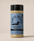 A 6oz bottle of Lake Spices Signature SPG Rub, featuring the company logo of a black loon on a blue-grey background, and a black icon of Minnesota in the upper righthand corner. Label text above the loon reads “Lake Spices: Honest Blends for Homemade Taste.”