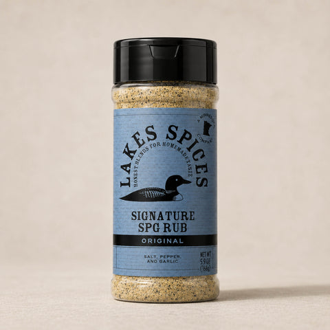 A 6oz bottle of Lake Spices Signature SPG Rub, featuring the company logo of a black loon on a blue-grey background, and a black icon of Minnesota in the upper righthand corner. Label text above the loon reads “Lake Spices: Honest Blends for Homemade Taste.”