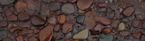 A close-up of smooth, polished river stones and pebbles, in shades of brown, reddish-brown, and gray.